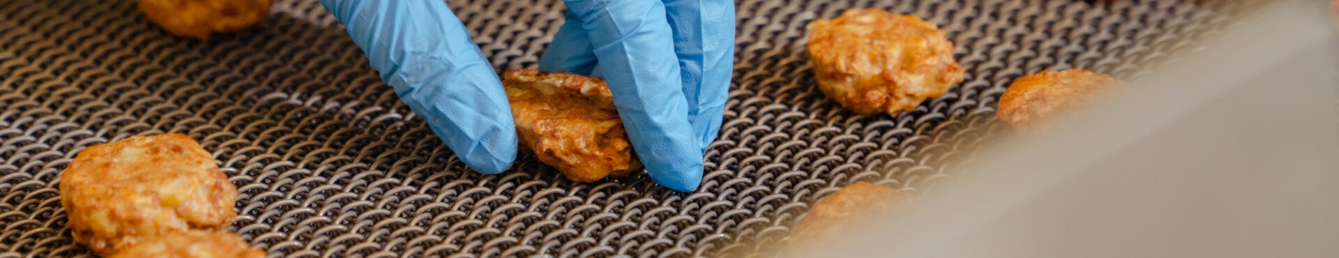 Qualitätskontrolle bei der Produktion von Frikadellen im Werk der Rügenwalder Mühle: Qualitätskontrolle per Hand am Fließband